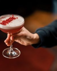 customer holding delicious pink freshly made raspberry milk punch cocktail in hand bar